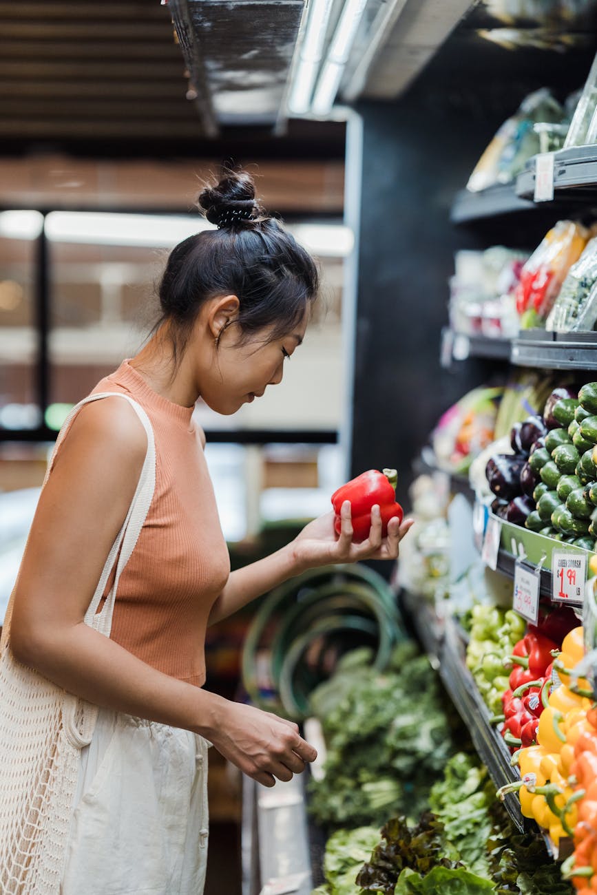 a woman holding a red bell pepper in a supermarket