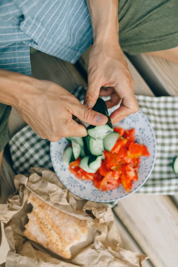 person holding white ceramic plate with sliced tomato and green vegetable